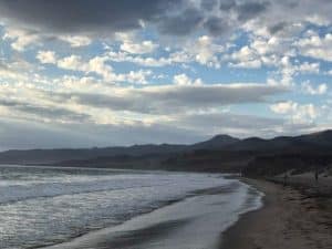 curved beach spans out the full length of the image, blue waves lap onto the sand.
