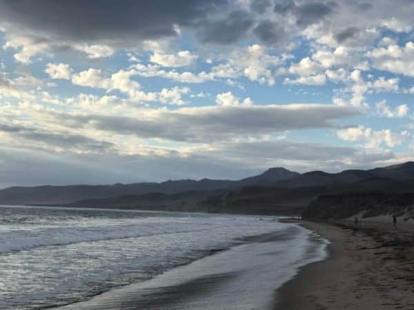 curved beach spans out the full length of the image, blue waves lap onto the sand.
