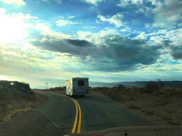 looking through the windscreen on the waay to jalama beach camping - the sky is bright blue with white clouds nd there's a white RV driving on the tarmac road ahead of us