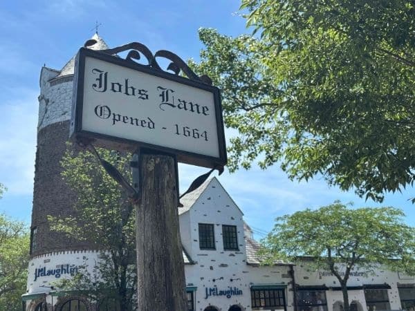 historic 1600s white buildings with trees in front. At the forefront a sign says "jobs lane, opened 1664"