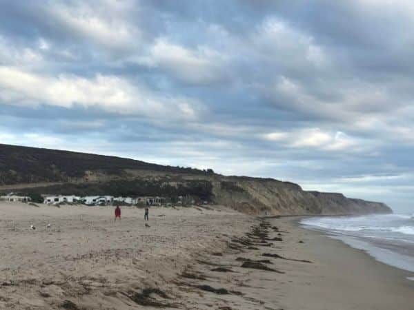 open expanse of jalama beach. cliffs at the fr end, RVs parked up behind the dunes.