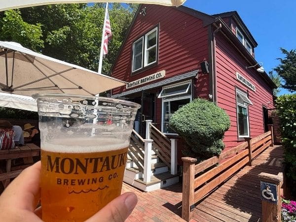 large red wooden building (montauk brewing company) stands behind a close up of a pint of beer