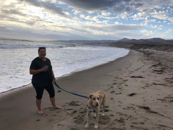 liz is walking Hana the golden lanrador long the jalama beach while holding a glass of wine